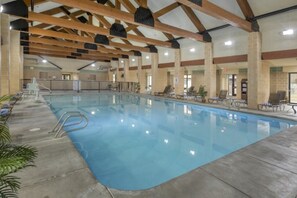 En indendørs swimmingpool med krystalklart vand, træbjælker og liggestole.
