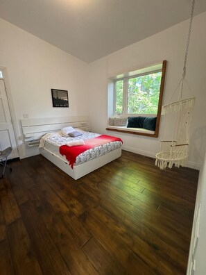 Een slaapkamer met een bed, een raam met uitzicht, een macramé fauteuil en een bureau.