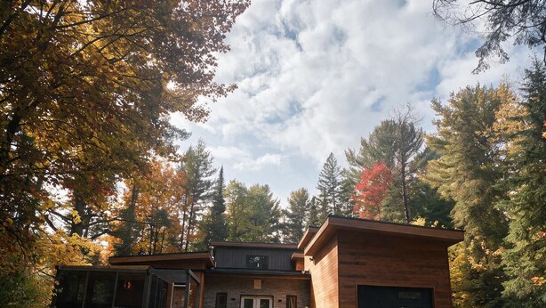 Eine zweigeschossige Blockhütte mit einer Veranda, einer Garage und einem gepflegten Rasen.