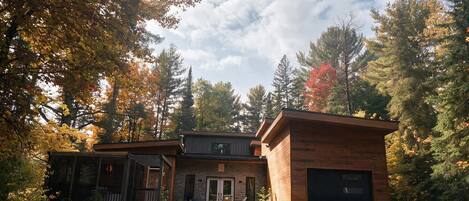Une cabane en rondins à deux étages, dotée d’un porche à l’avant, d’un garage et d’une pelouse bien entretenue.