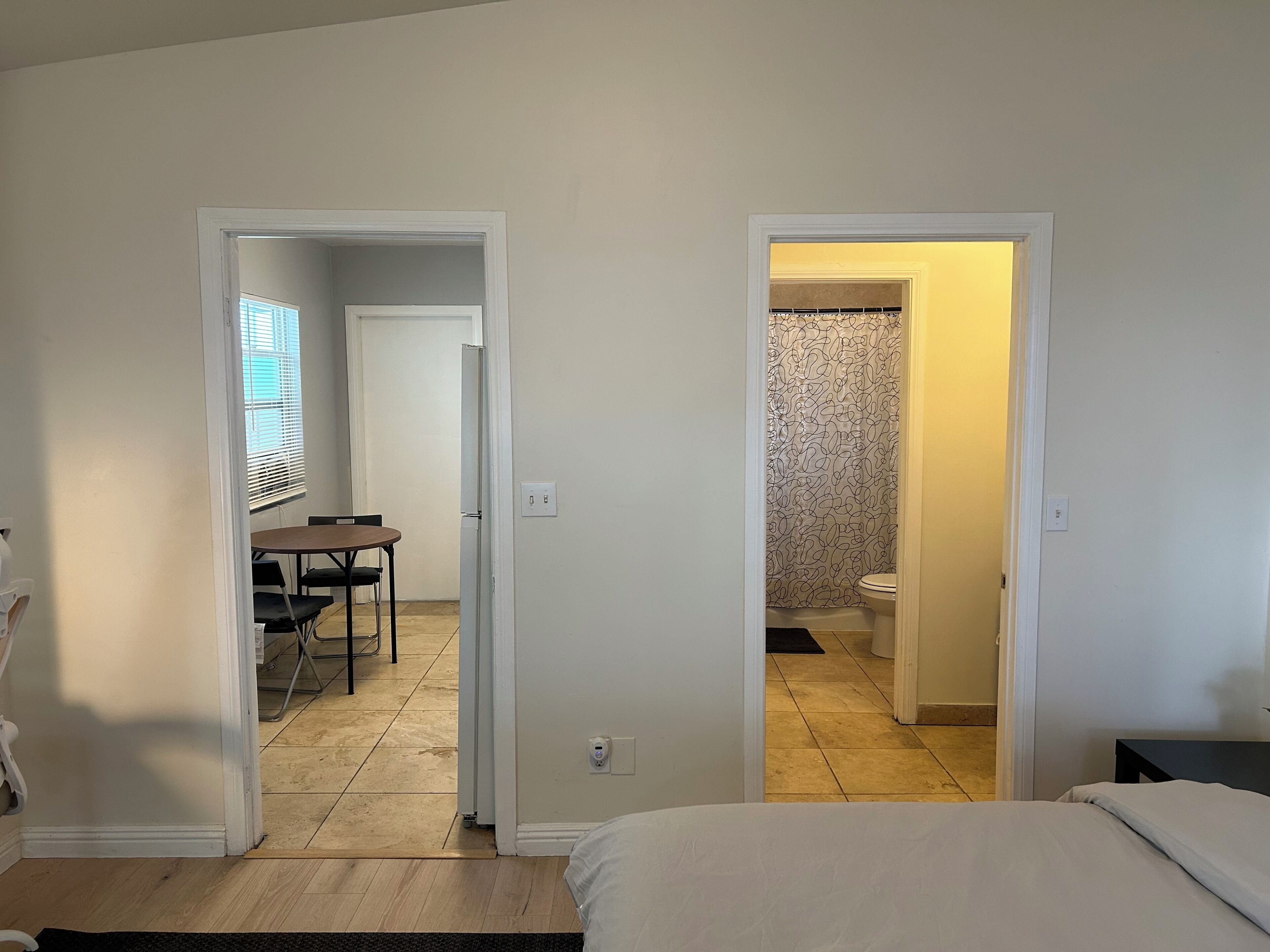 Une chambre avec un lit, une salle de bain avec des toilettes et une douche, et un coin repas avec une table et des chaises.