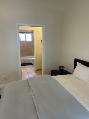 Une chambre à coucher avec un lit, une table de chevet et une vue sur la salle de bain par une porte ouverte.