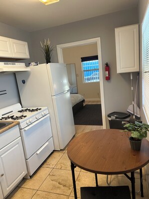 A kitchen with white cabinets, a stove, a refrigerator, and a dining table with a plant. - F, Comfy Studio in Vibrant DTLA (Los Angeles)