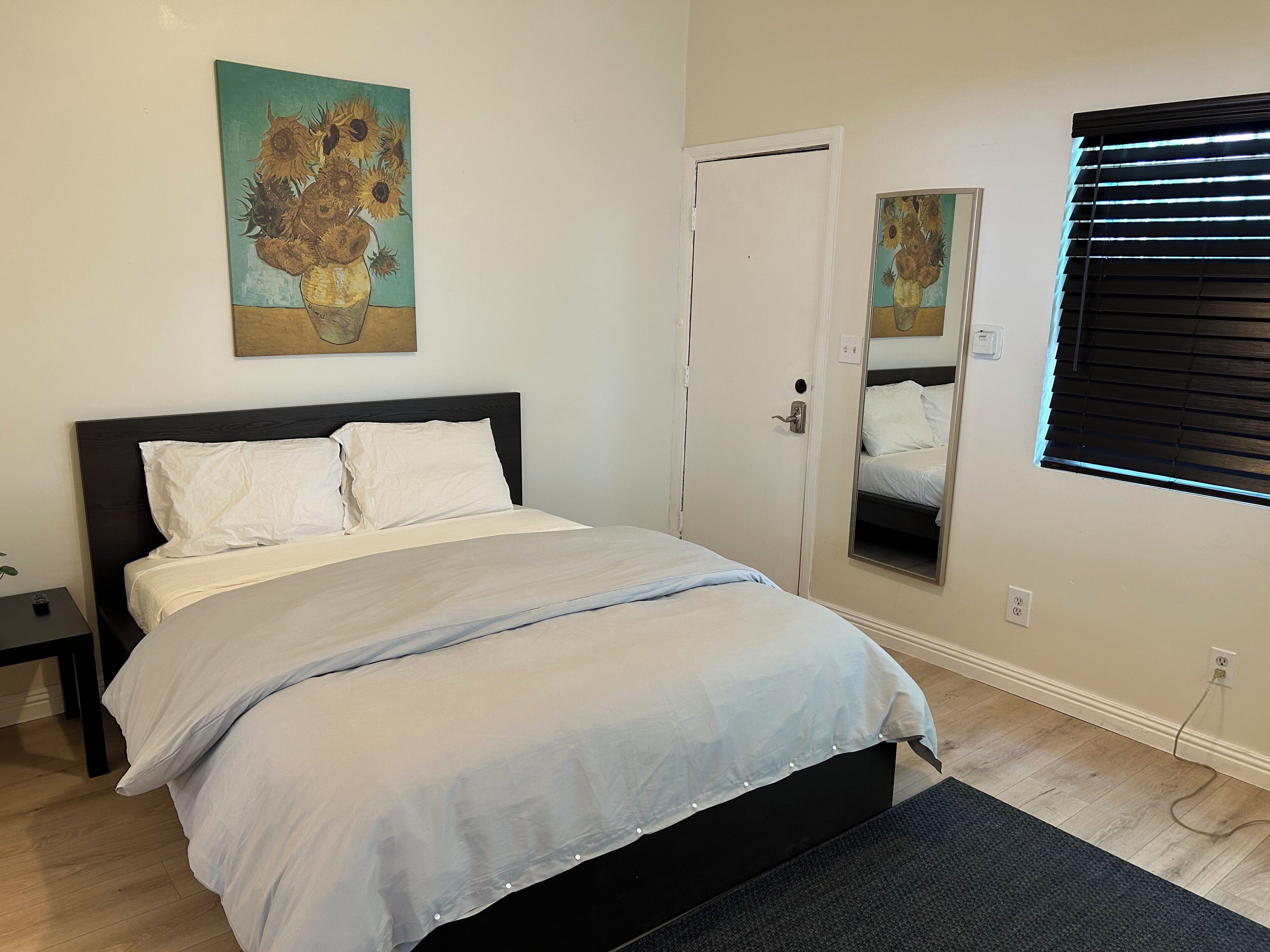 A bedroom with a bed, a bedside table, a mirror, and artwork on the wall.