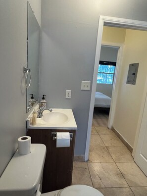 A bathroom with a sink, toilet, and a mirror. There is a towel rack and a bottle of soap. The walls are painted in a light color, and the floor is tiled. - F, Comfy Studio in Vibrant DTLA (Los Angeles)