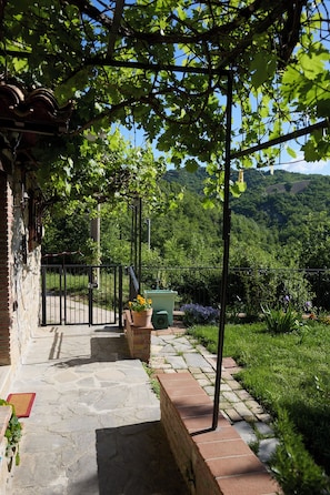Ein gepflasterter Weg führt zu einer überdachten Terrasse mit Blick auf eine üppige grüne Landschaft und Hügel.