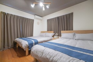 Una habitación de hotel con dos camas, un cabecero de madera, una mesita de noche con un florero y un ventilador de techo.