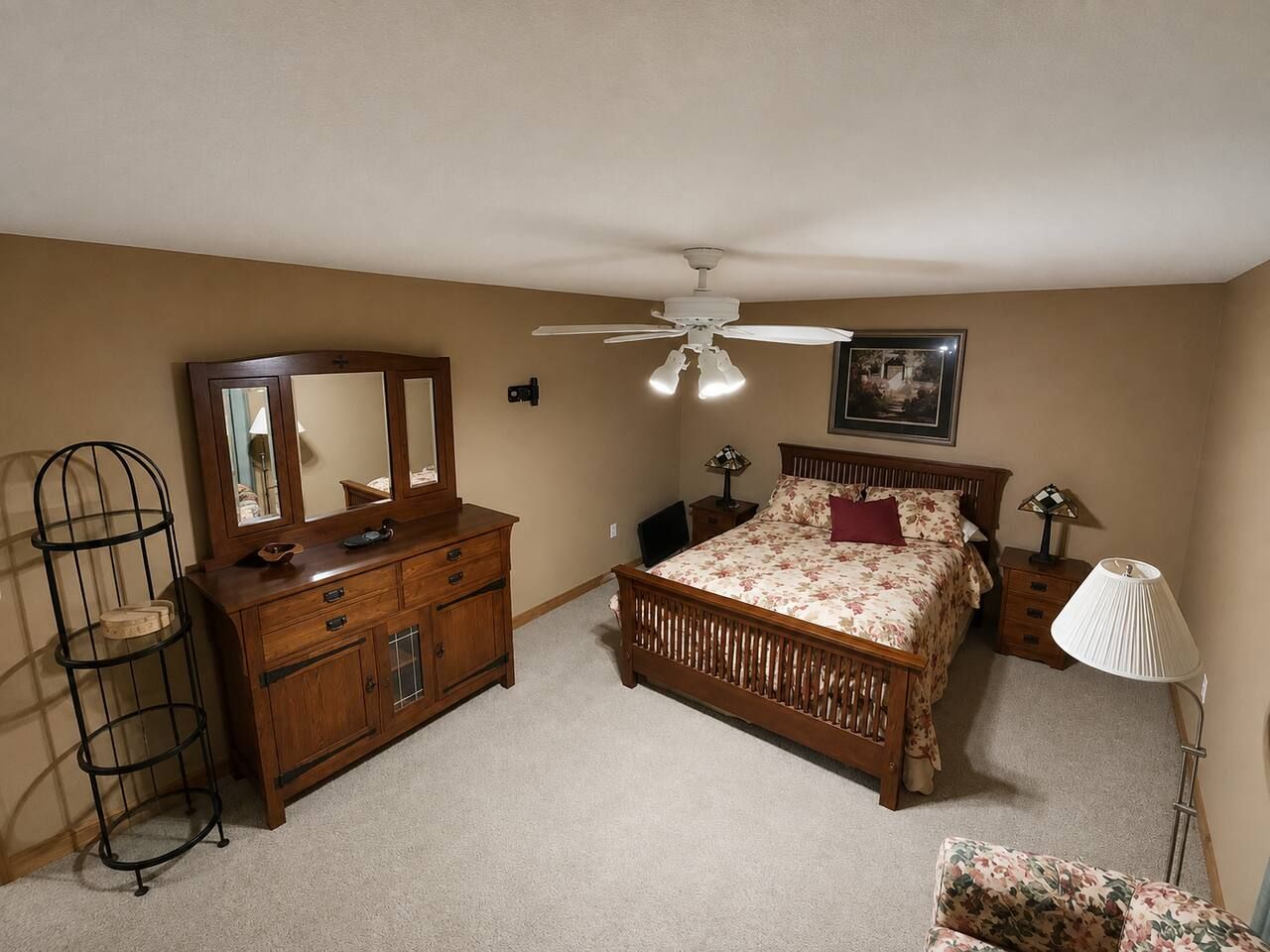 Une chambre à coucher comprenant un lit, une commode, un miroir, un ventilateur de plafond, une lampe et une chaise.