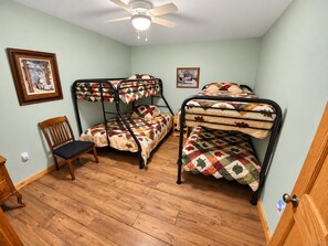 A room with three bunk beds, a wooden chair, and two framed pictures on the wall. - Manny's Lakeside Lodge (Mercer)
