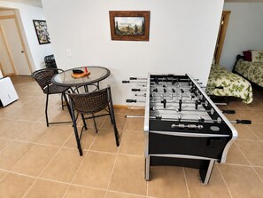 A room with a foosball table, a round table with chairs, and a bed with a floral bedspread. - Manny's Lakeside Lodge (Mercer)