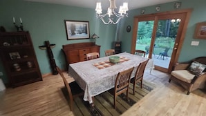 Een eetruimte met een tafel voor vier personen, omringd door houten stoelen, een kroonluchter en een uitzicht door een glazen deur naar buiten.