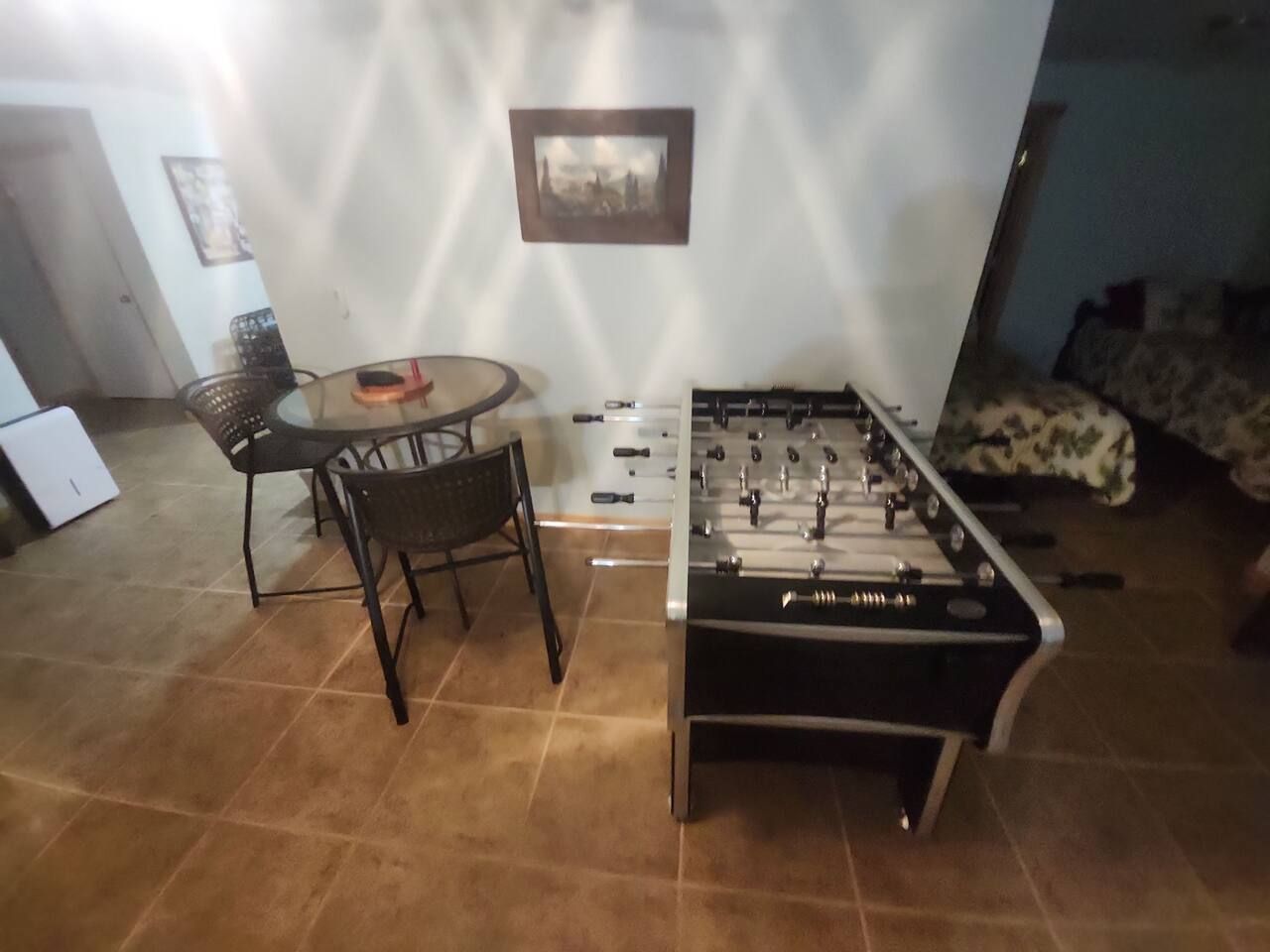 Ein Zimmer mit einem Kicker, einem Esstisch mit Stühlen und einer Couch.