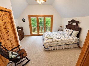 A bedroom with a bed, a chair, a dresser, and a window with a view of greenery. - Manny's Lakeside Lodge (Mercer)
