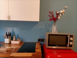 A kitchen with a microwave on a red stand, a wooden countertop, and a vase with red berries and cotton on the wall. - Apartment in Pomposa, in the heart of the city (Modena)
