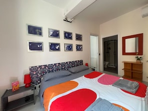 A bedroom with a bed, nightstand, lamp, and a wall with framed artwork. - Apartment in Pomposa, in the heart of the city (Modena)