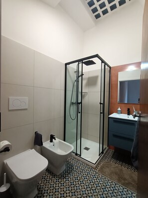A modern bathroom with a glass-enclosed shower, a bidet, a toilet, and a sink with a mirror. - Vrbo Property (Modena)