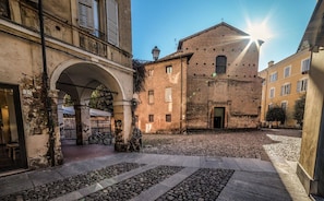 A courtyard with cobblestone flooring, a historic building with a brick facade, and an archway leading to a building with a balcony. - Vrbo Property (Modena)