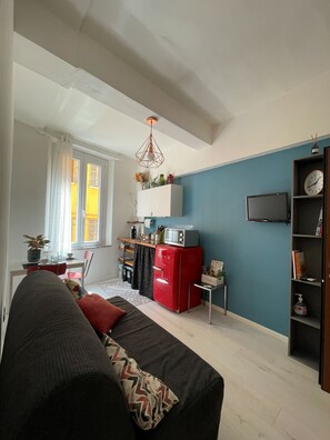 A living room with a sofa, a red refrigerator, a television, and a kitchen area with a window. - Apartment in Pomposa, in the heart of the city (Modena)