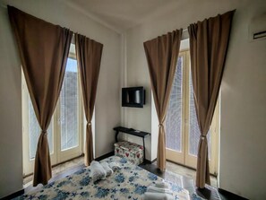 A hotel room with a bed, curtains, a television, and a small table. - A lane of dreams—nature, art, the sea, and the city—nothing could be more complete (Salerno)