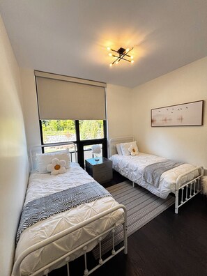 A bedroom with two single beds, a window with a view, a ceiling light fixture, and a framed picture on the wall. - Your Friday Harbour Escape Awaits! (Innisfil)