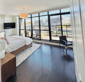 A modern bedroom with a large window, a bed, a chair, and a TV. - Your Friday Harbour Escape Awaits! (Innisfil)