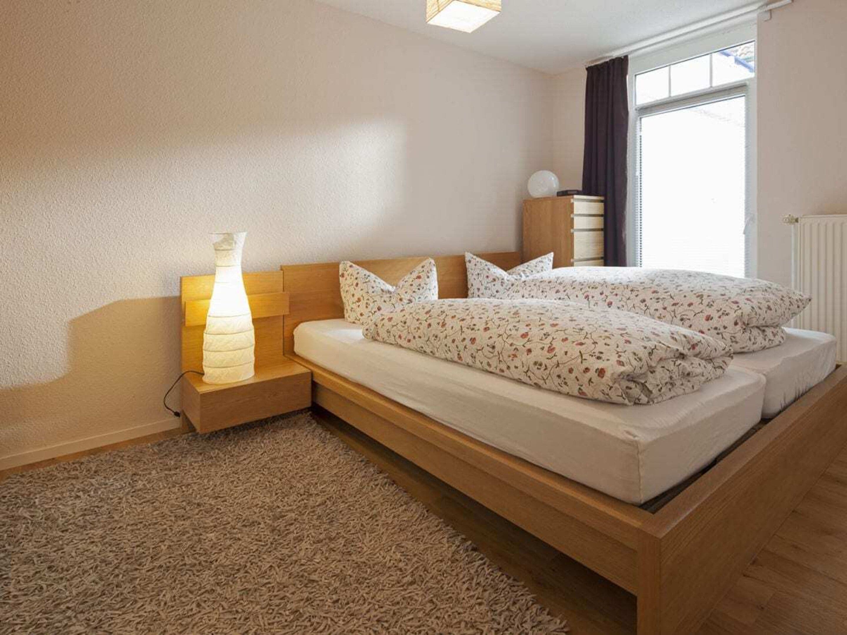 Une chambre à coucher avec un lit, une lampe de chevet et une fenêtre avec des rideaux.