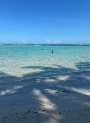 A beach with clear turquoise water, a sandy shore, and a distant pier. - Bright 2-bedroom apartment with AC in tranquil Boca Chica (Boca Chica)