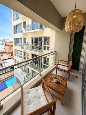 A balcony with a view of a swimming pool, a wooden table with a cushion, and a hanging light fixture. - Bright 2-bedroom apartment with AC in tranquil Boca Chica (Boca Chica)