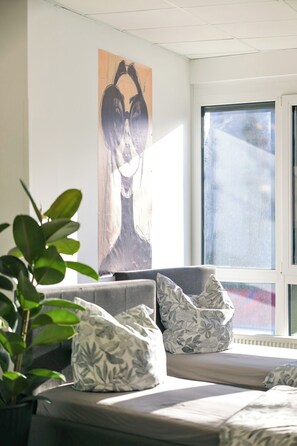 Ein Zimmer mit einem großen Fenster, einer Couch mit gemusterten Kissen und einem Wandbild.