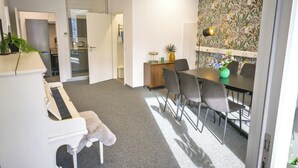 Uma sala de conferências com um piano, uma mesa com cadeiras e um vaso decorativo.