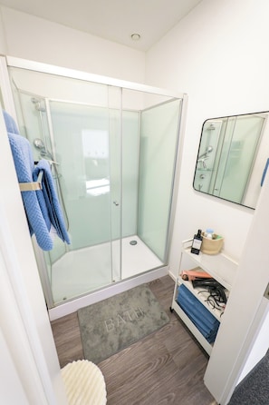 Ein modernes Badezimmer mit einer einteiligen Duschkabine, einem weißen Waschbecken mit Spiegel darüber und einem kleinen Ablagefach für Toilettenartikel.