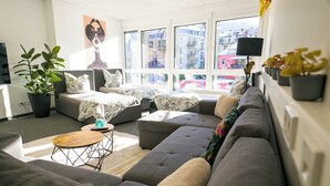 Uma sala de estar moderna com um sofá seccional cinza, uma mesa de centro redonda e uma grande janela com vista para edifícios.