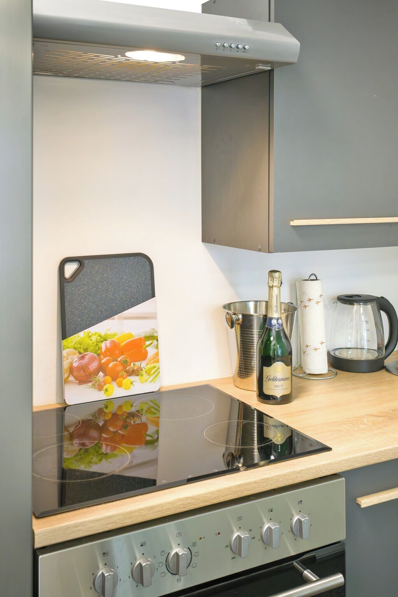 Eine Küche mit einer schwarzen Induktionskochplatte, einem Edelstahlbackofen und einer Holzausziehtafel.