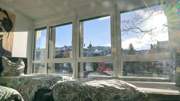 A room with two beds, large windows, and a view of a town.