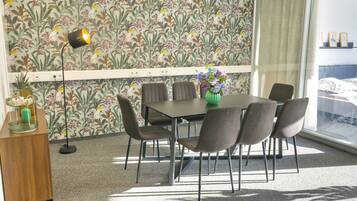 A dining area with a table and chairs, a vase with flowers, and a wall with a floral pattern.
