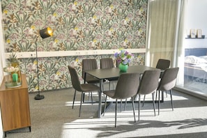 A dining area with a table and chairs, a vase with flowers, and a wall with a floral pattern.