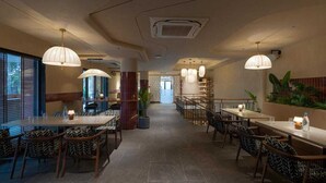 Un restaurante con varias mesas y sillas, un pasillo central y lámparas colgantes.