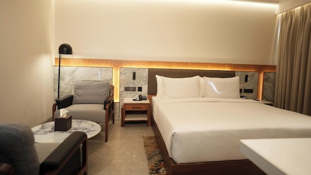 Una habitación de hotel con una cama, una silla, una mesita de noche y una lámpara.