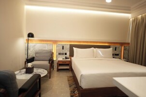 Una habitación de hotel con una cama, una silla, una mesita de noche y una lámpara.