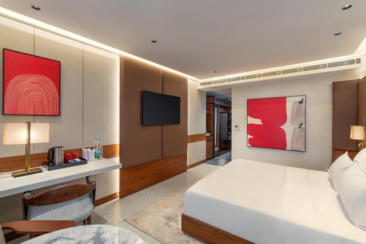 A modern hotel room with a bed, a desk, a chair, and a television.