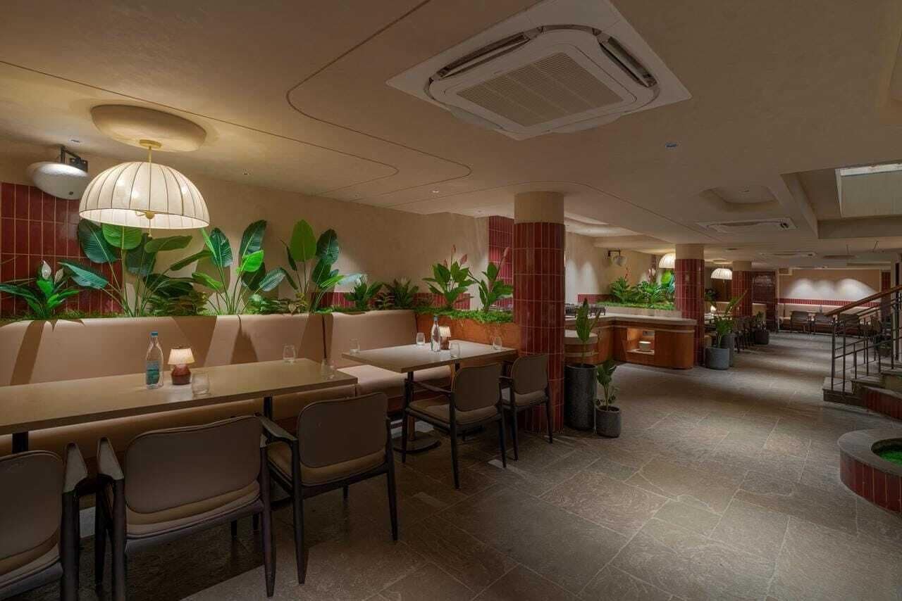Um restaurante com cabines e mesas, plantas internas e uma escada.