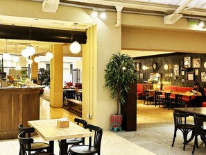En restauranginteriör med en bardisk, sittplatser och en stor krukväxt.