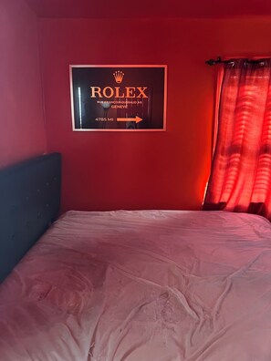 Een kamer met een bed, een bord aan de muur met het Rolex-logo, en een gordijn.