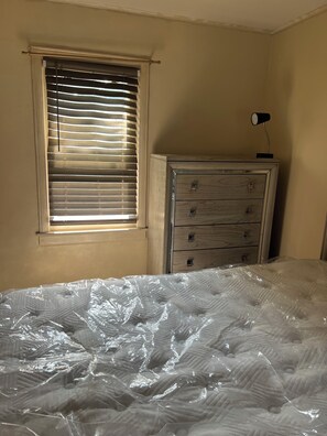 Een kamer met een bed, een dressoir en een raam met jaloezieën.