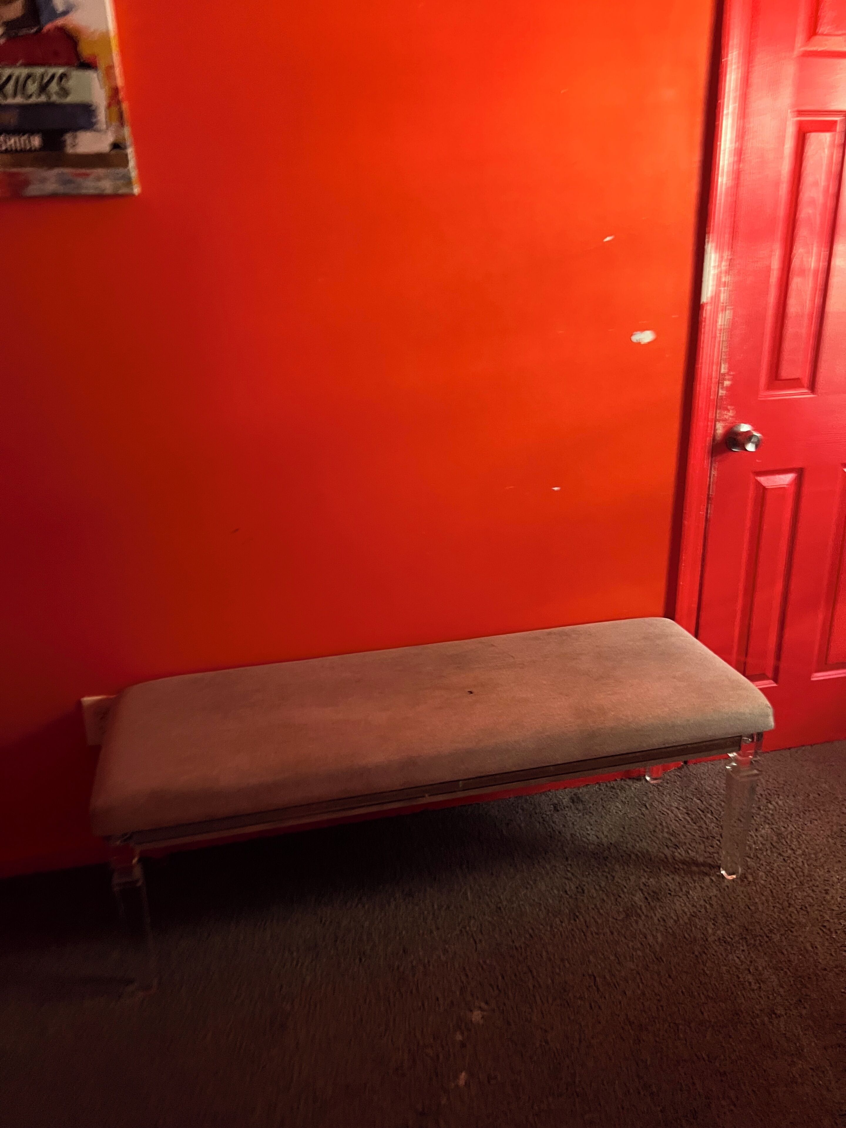 Un banc dans une pièce avec une porte rouge et une affiche accrochée au mur.
