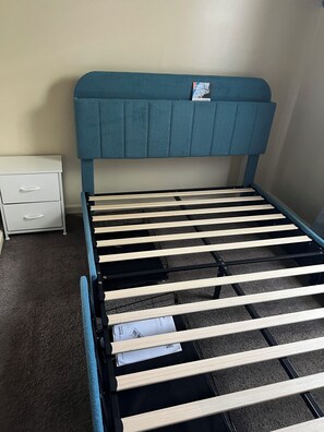 A bed with a headboard, a white nightstand with drawers, and a carpeted floor.