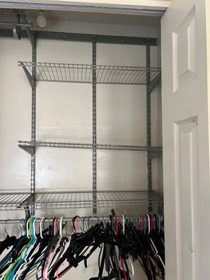 A closet with metal shelving units and a rack of hanging clothes.