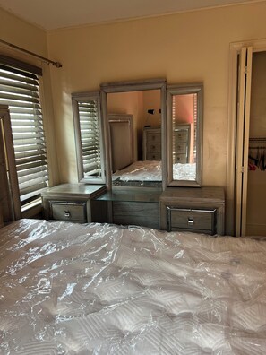 Een slaapkamer met een groot bed, een dressoir met lades, een spiegel en een kledingkast.