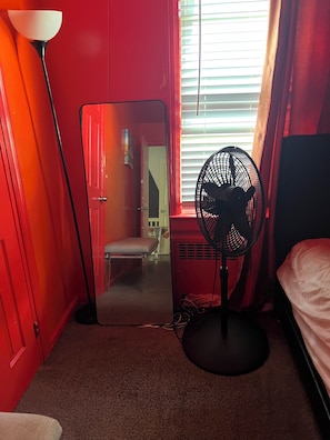 Een kamer met een rode wand, een bed, een ventilator en een vloerlamp.