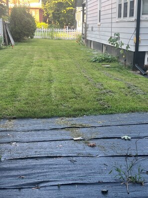 A backyard with a wooden deck, a white fence, and a house in the background.